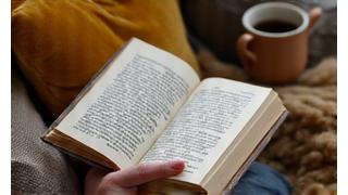 Someone reading a book in a cozy, sunlit armchair with a cup of tea, representing relaxation and digital detox.